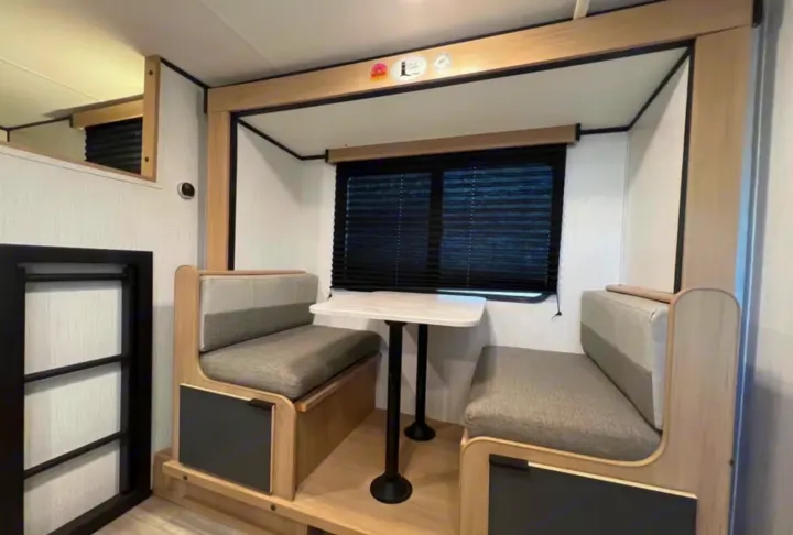 Cozy **RV rental** dinette with window, table, two benches, and access to **bunk beds**. Modern, light-toned interior.. Cruiser RV Hitch 2022