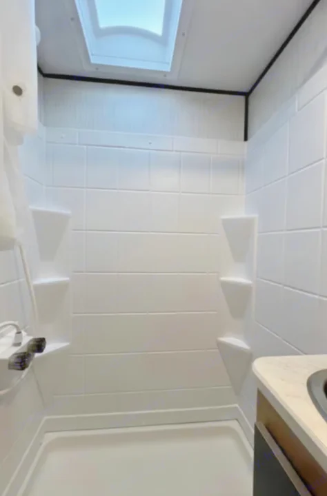 Clean, compact shower with skylight in an RV rental bathroom. Features white tiled walls and corner shelves.. Cruiser RV Hitch 2022