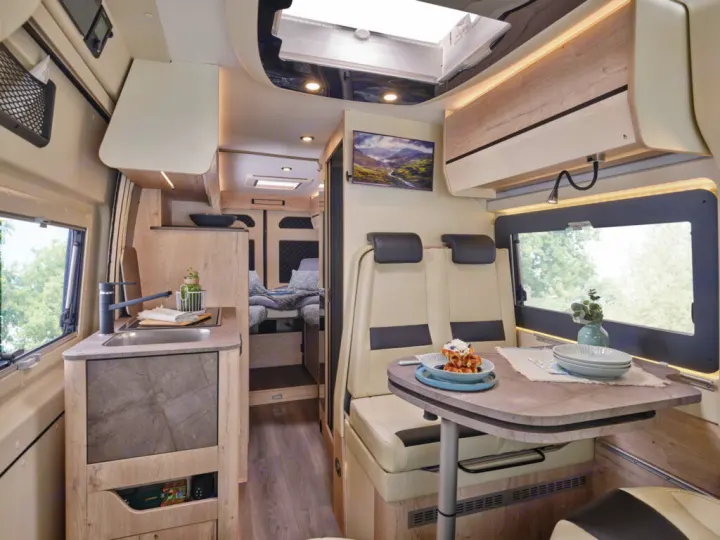 RV rental interior: A bright camper van with a modern kitchen, dining area (waffles on table), and a comfortable rear bed.. FLORIUM BLACK PEARL 63 LJ 2025