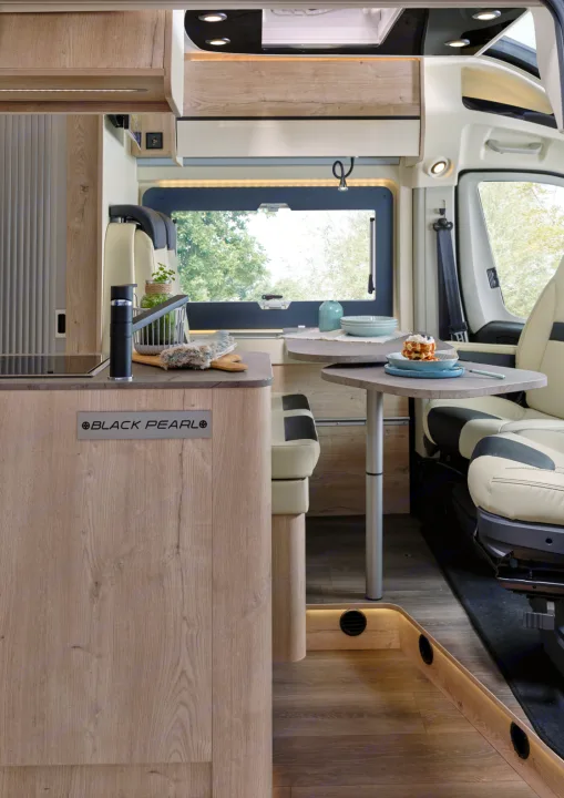 Modern RV rental interior featuring a compact kitchen with a sink, dining area with seating, and a scenic window view.. FLORIUM BLACK PEARL 63 LJ 2025
