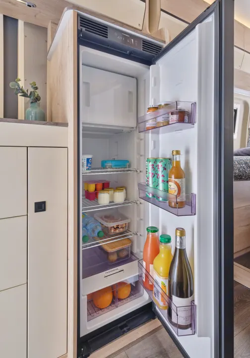 Open Dometic RV fridge, fully stocked for an rv rental adventure: yogurts, drinks, snacks, and oranges on shelves and in door bins.. FLORIUM BLACK PEARL 63 LJ 2025