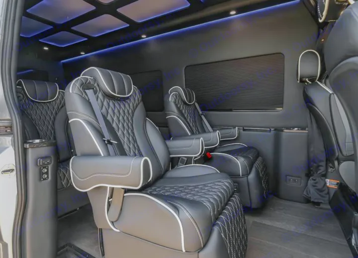 Inside a luxurious rv rental: plush black quilted leather seats with white trim, blue mood lighting, and dark wood-look floor.. Mercedes Benz by Legends Sprinter 3500xd 170 Ext AWD Executive Lounger 2023