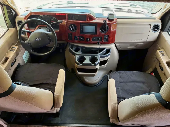 RV rental cockpit interior showing Ford dashboard, steering wheel, stereo, cup holders, and two front seats with covers.. Winnebago Chalet 2014
