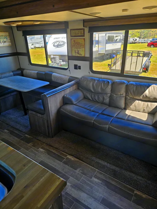 RV rental interior: A cozy living space featuring a dark sofa, a light-wood dinette, and bright windows with outdoor views.. KZ Sportsman 2022