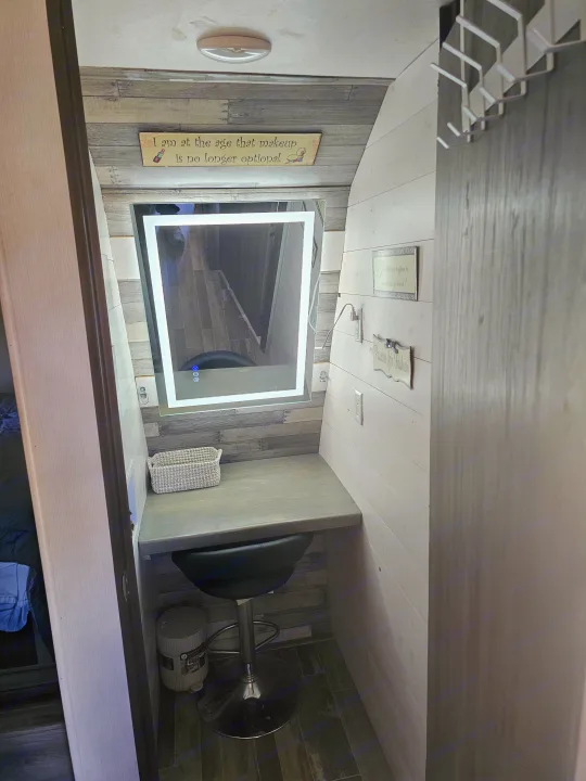 Experience a compact RV rental vanity with an illuminated mirror, wooden paneling, and a comfy stool for your makeup.. KZ Sportsman 2022