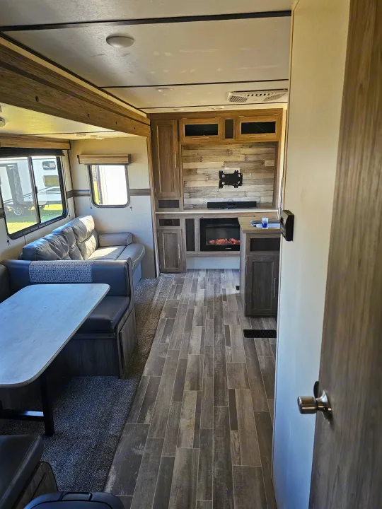Spacious, modern RV rental interior featuring a comfortable dinette, sofa, and entertainment center with a fireplace. Perfect for travel!. KZ Sportsman 2022