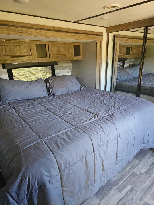 Spacious RV rental bedroom featuring a bed with grey bedding, wood-look overhead cabinets, and a mirrored closet.. KZ Sportsman 2022