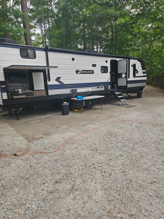 This Zinger travel trailer RV rental offers an outdoor kitchen setup at a wooded campsite, perfect for your next adventure.. KZ Sportsman 2022