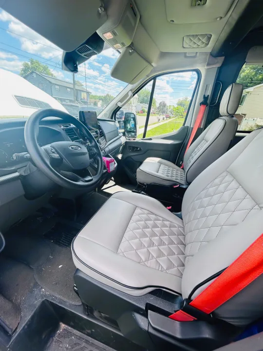 Spacious Ford van interior for rv rental: light grey quilted seats, dashboard view, and bright red seatbelts detail the front cabin.. Primetime Avenger 2021