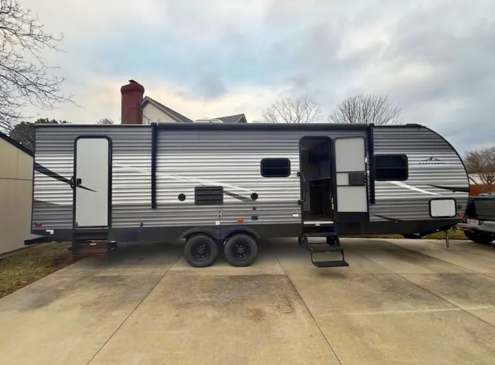 This gray & black RV rental travel trailer is parked on a driveway. Its main entry door is open with steps extended.. East to West Silver Lake 2021