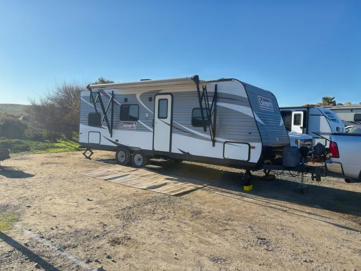A Coleman travel trailer RV rental, with an awning and leveling jacks, is parked on a sunny dirt lot.. Coleman Lantern 2018