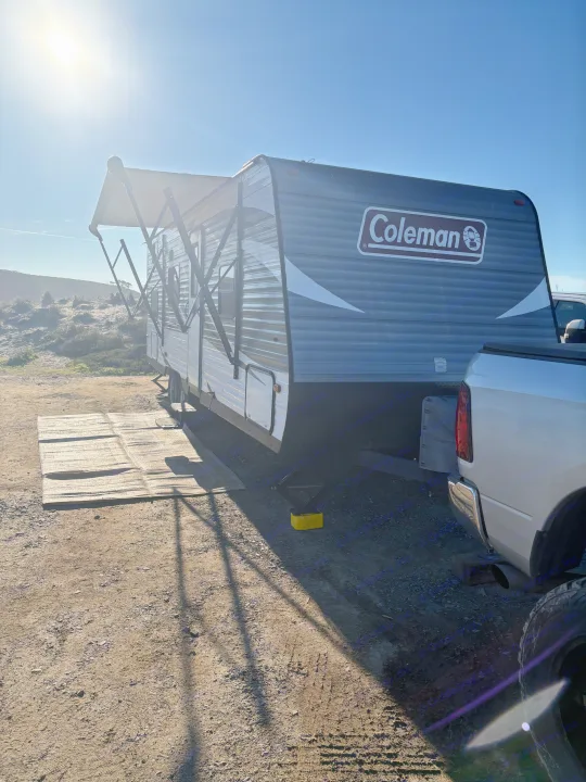 This bright, sunny rv rental shows a Coleman travel trailer with an awning extended, hitched to a pickup truck at a dusty campsite.. Coleman Lantern 2018