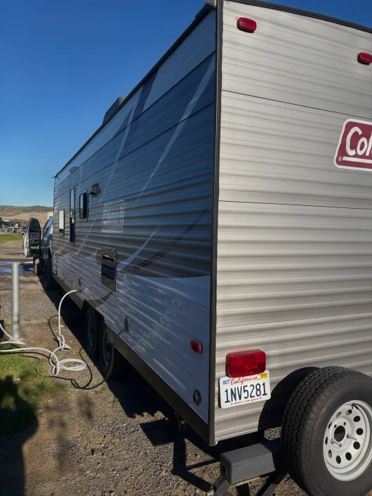 Gray Coleman RV rental trailer with California plate, parked at campsite, a hose connected to its side.. Coleman Lantern 2018