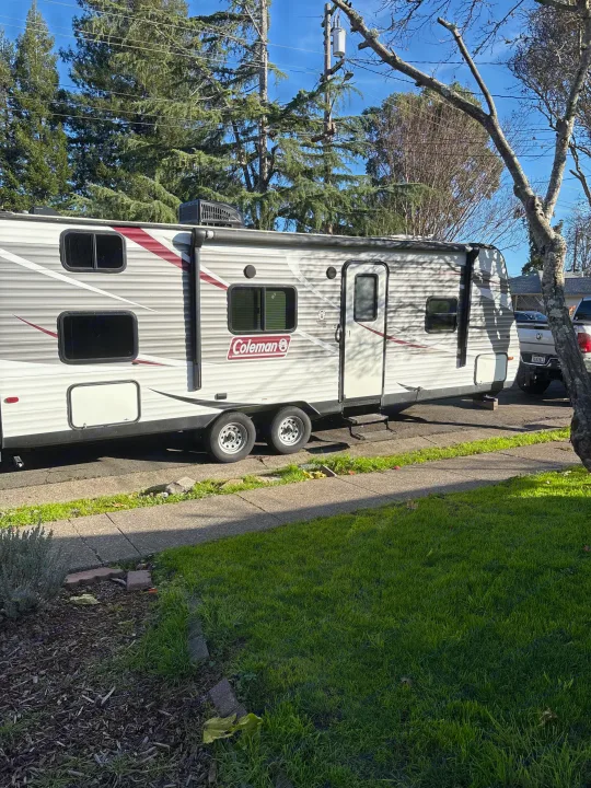 A Coleman travel trailer, ideal for an RV rental, is parked curbside on a sunny day, showcasing its white and maroon design.. Coleman Lantern 2018
