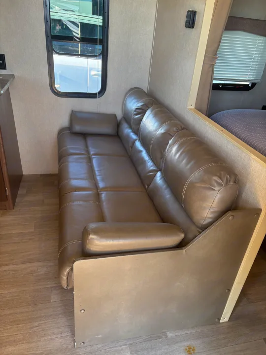 Cozy RV rental interior with a brown faux leather sofa, side window, and glimpse of the sleeping area.. Coleman Lantern 2018