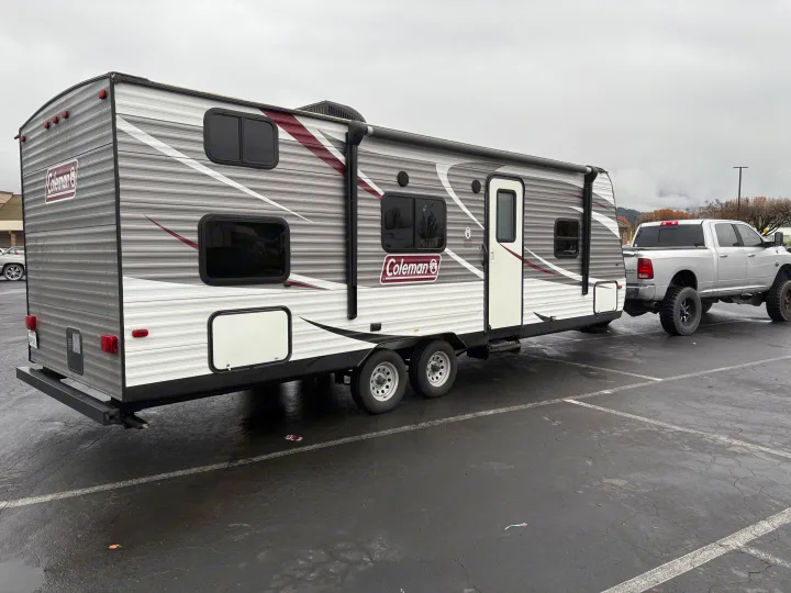 Coleman RV rental, a travel trailer, hitched to a silver pickup truck in a paved lot under an overcast sky.. Coleman Lantern 2018