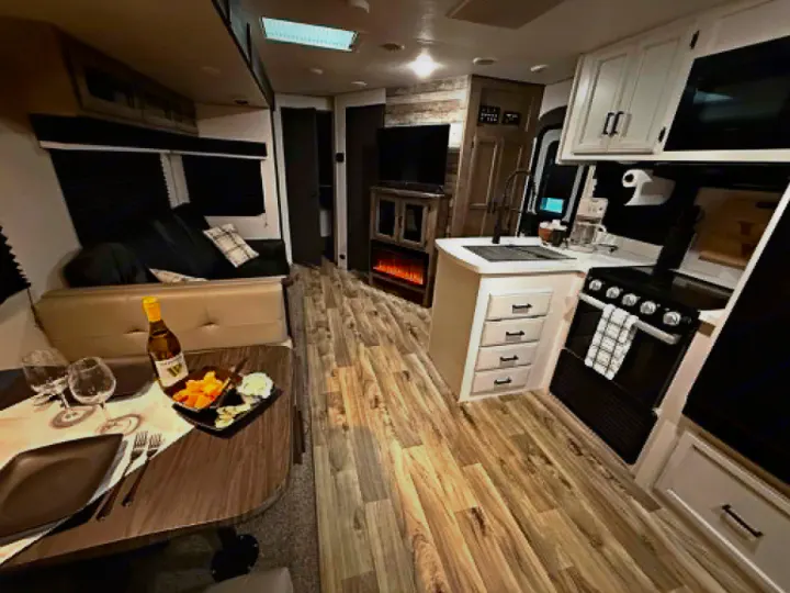 This cozy rv rental interior shows a set dining table, modern kitchen, living area with sofa, and electric fireplace.. Venture Other 2022