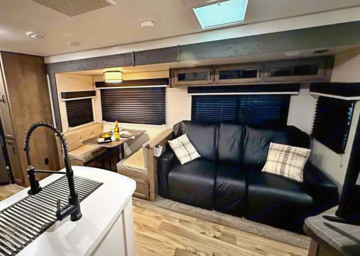 RV rental's inviting interior: kitchen island, dining booth, and black sofa with plaid pillows for comfortable travel.. Venture Other 2022