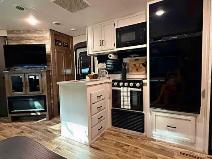 Spacious rv rental interior featuring a modern kitchen, built-in appliances, island, living area with TV & fireplace.. Venture Other 2022