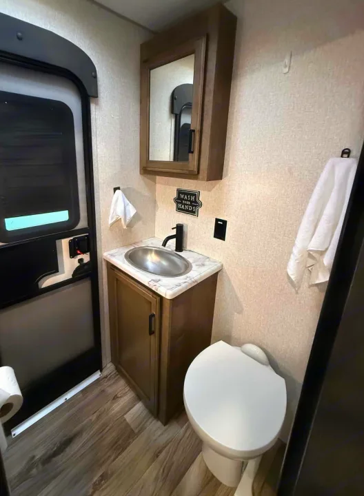 RV rental bathroom features a compact modern vanity with a silver sink, mirror, and toilet, all on a wood-look floor.. Venture Other 2022
