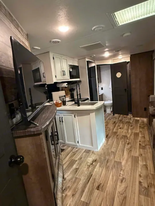 Modern RV rental interior: a kitchen island, wood floors, flat-screen TV, and open bathroom door with toilet visible.. Venture Other 2022