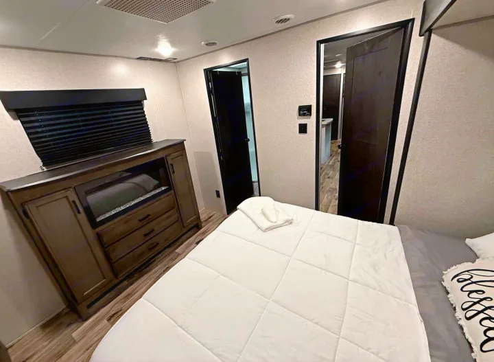 Inviting RV rental bedroom with a comfy bed, "blessed" pillow, wood dresser, and dark doors, offering cozy travel.. Venture Other 2022
