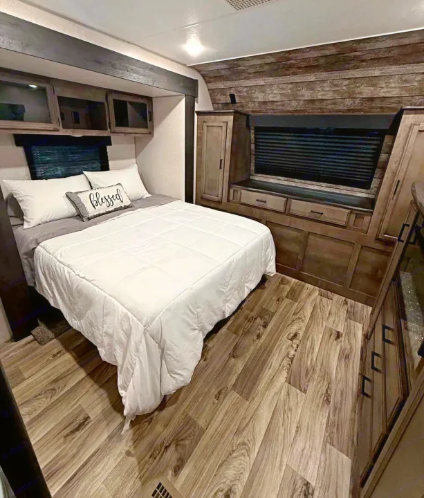 Cozy RV rental bedroom featuring a comfy bed with "Blessed" pillow, overhead storage, wood-look floor, and warm wood accents.. Venture Other 2022