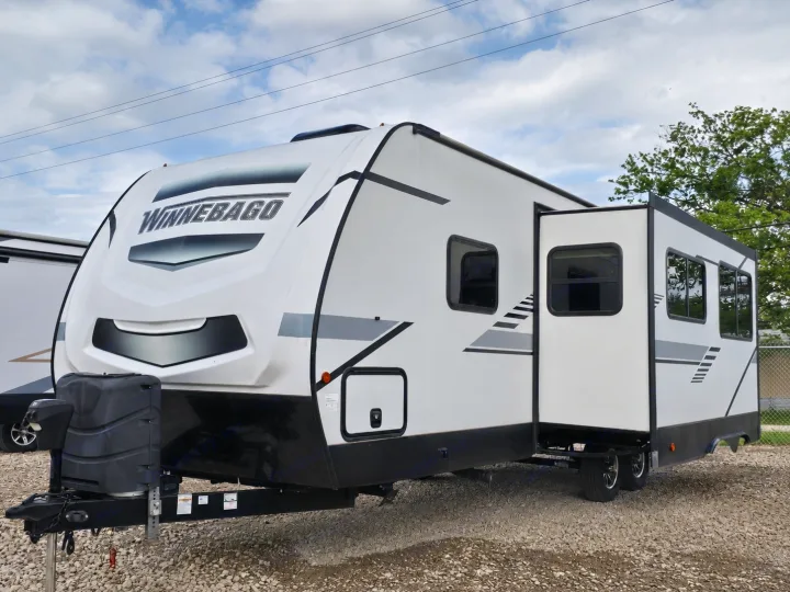 This white Winnebago travel trailer, with its slide-out extended, is pictured outdoors on gravel for rv rental.. Minnie Minnie Trailer 2022