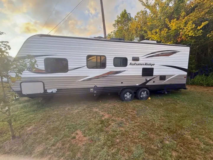 Autumn Ridge travel trailer for RV rental, parked on a grassy hill under a cloudy sky, with trees nearby.. Starcraft Autumn Ridge Outfitter 2018