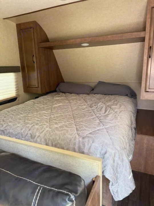 RV rental bedroom with a comfortable bed, gray bedding, overhead storage, and a partial view of a sofa.. Starcraft Autumn Ridge Outfitter 2018