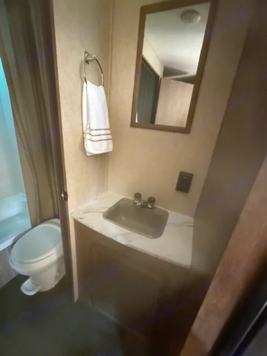 Compact RV rental bathroom features a toilet, sink vanity with a mirror, and a towel on a ring.. Starcraft Autumn Ridge Outfitter 2018