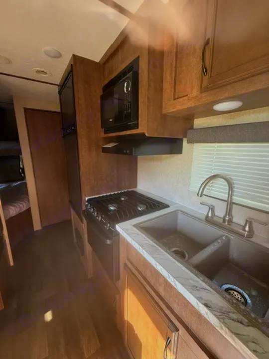 Explore this RV rental kitchen with a compact microwave, gas stove, dual sink, & fridge. Essential amenities for your road trip.. Starcraft Autumn Ridge Outfitter 2018