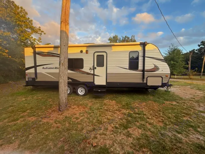 An Autumn Ridge RV rental, a travel trailer, sits on grass, partly hidden by a pole. Perfect for outdoor getaways!. Starcraft Autumn Ridge Outfitter 2018