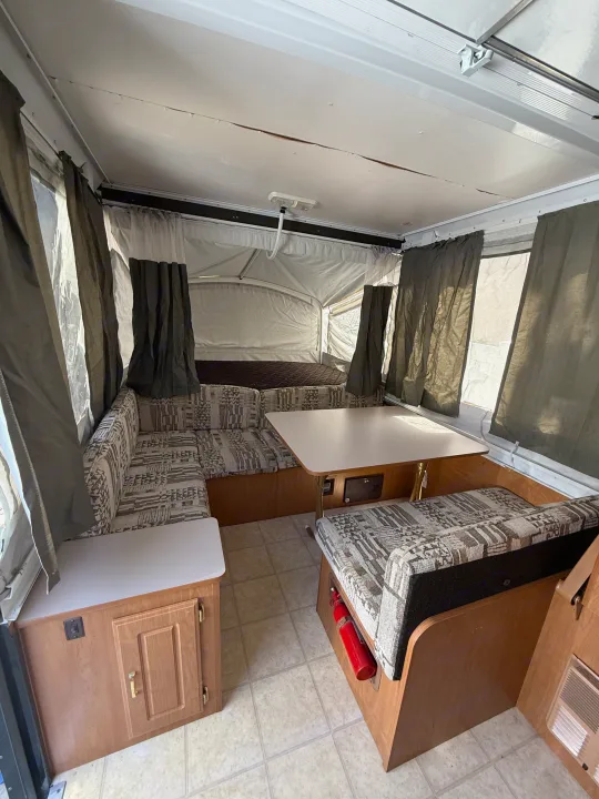 Pop-up camper RV rental interior, featuring a dinette with patterned cushions, bed area, and privacy curtains.. Coleman Grand Tour 2003