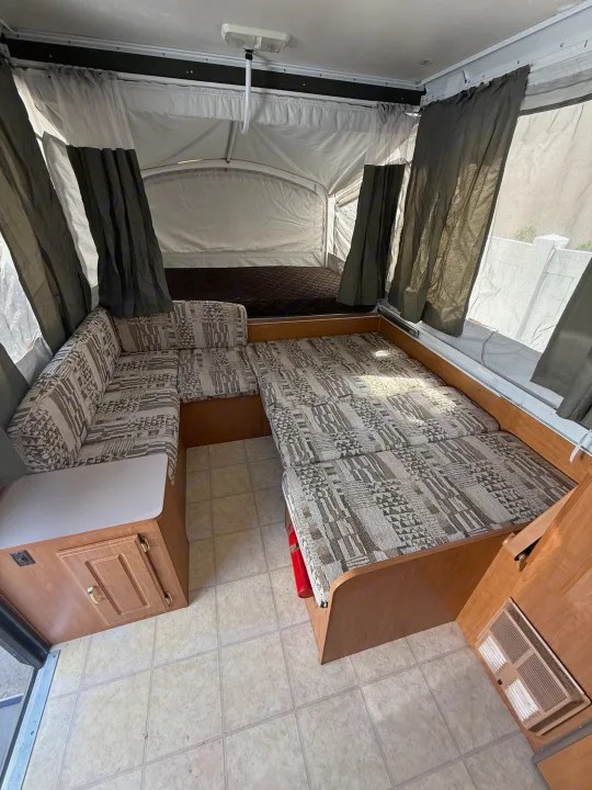 This RV rental offers a pop-up camper interior featuring a convertible dinette bed, additional bunk, and practical tiled floor.. Coleman Grand Tour 2003