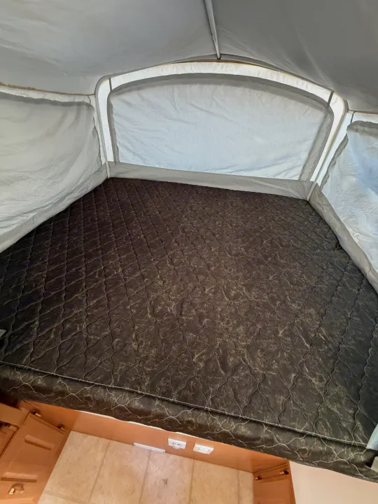 Interior of an RV rental pop-up camper, featuring a dark, quilted mattress in a fabric-walled sleeping area with wooden trim.. Coleman Grand Tour 2003