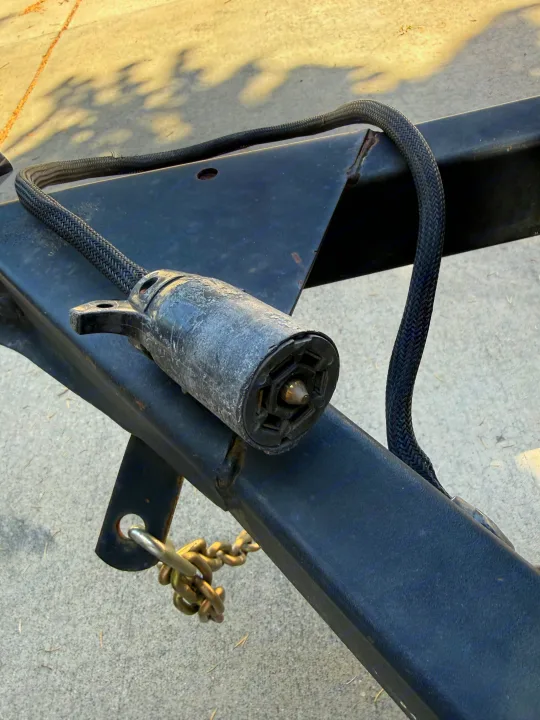 Close-up of an RV rental 7-pin trailer electrical connector with braided wiring and safety chain on the hitch for vehicle connection.. Coleman Grand Tour 2003