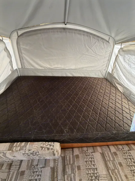 Cozy pop-up camper bed in an RV rental, featuring a dark quilted mattress and canvas walls, ready for your adventure.. Coleman Grand Tour 2003