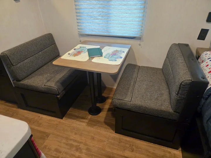 This RV rental features a compact dinette with gray upholstered booth seating, a light wood table, and window blinds.. Forest River Cherokee Wolf Pup 2022