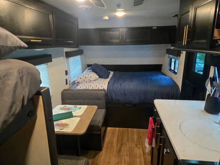 Cozy RV rental interior: bed, dining booth, kitchen counter, dark cabinets. Compact living with bunk bed partially visible.. Forest River Cherokee Wolf Pup 2022