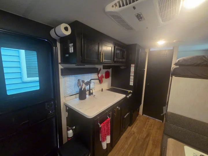 Modern RV rental kitchen with dark cabinets, light countertop, microwave, fridge, and a glimpse of the sleeping area.. Forest River Cherokee Wolf Pup 2022