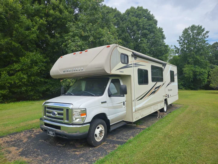 White Winnebago Class C RV rental parked on a driveway with a cat nearby, lush green lawn and trees in the background.. Winnebago Minnie Winnie 2019