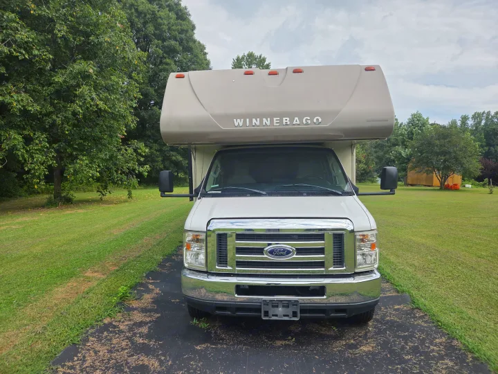 Front view of a white Ford Winnebago Class C RV parked on a driveway with green grass and trees. Great for your next rv rental!. Winnebago Minnie Winnie 2019