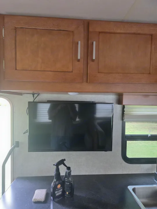 RV rental interior features: wooden cabinets, mounted TV, dark counter with cleaning supplies, sink, and window view.. Winnebago Minnie Winnie 2019