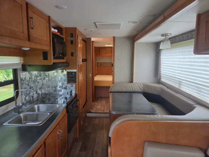Bright rv rental interior with kitchen (sink, stove, microwave), U-shaped dinette, and rear bedroom entrance.. Winnebago Minnie Winnie 2019