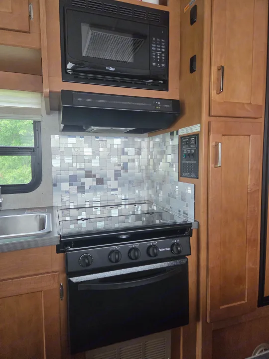 Compact RV rental kitchen with High Pointe microwave, Suburban stove/oven, sink, and control panel. Modern tile backsplash completes the functional space.. Winnebago Minnie Winnie 2019