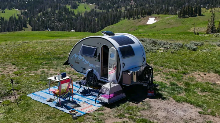 Teardrop RV rental set up for off-grid camping in a scenic mountain meadow with pine trees and snow patches.. nuCamp T@B 2022