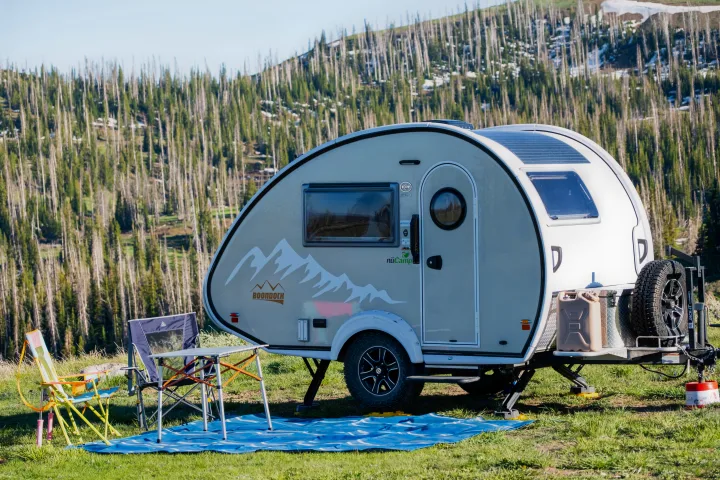 This nuCamp Boondock teardrop rv rental is set up for camping, with solar panels, chairs, and a table in a mountain forest.. nuCamp T@B 2022