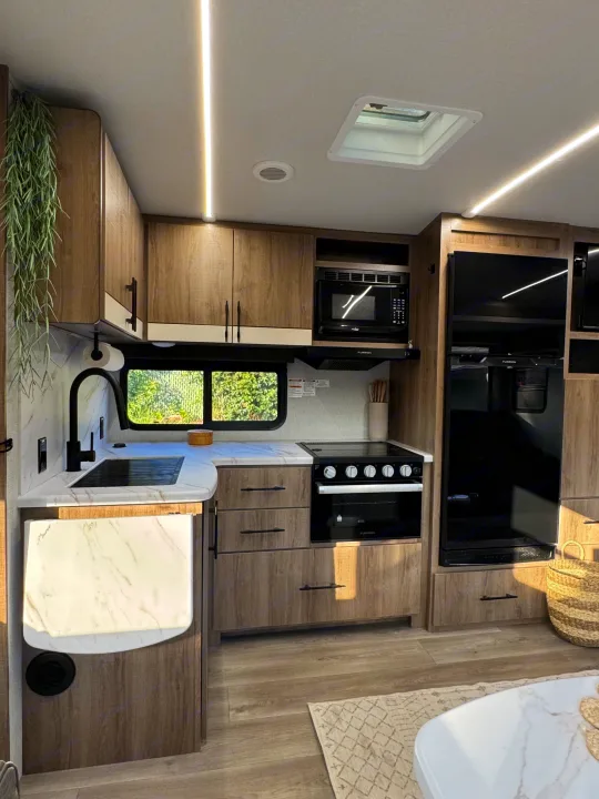 Bright rv rental kitchen: sleek wood cabinetry, marble-look counters, black appliances, and a skylight for natural light.. Grand Design Imagine 2025
