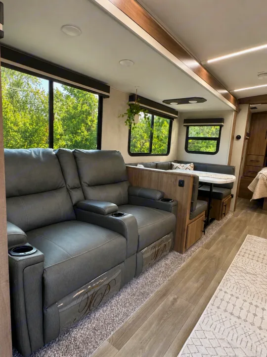 Spacious rv rental interior features comfy recliners, a dinette, and large windows with scenic green views. Modern design throughout.. Grand Design Imagine 2025